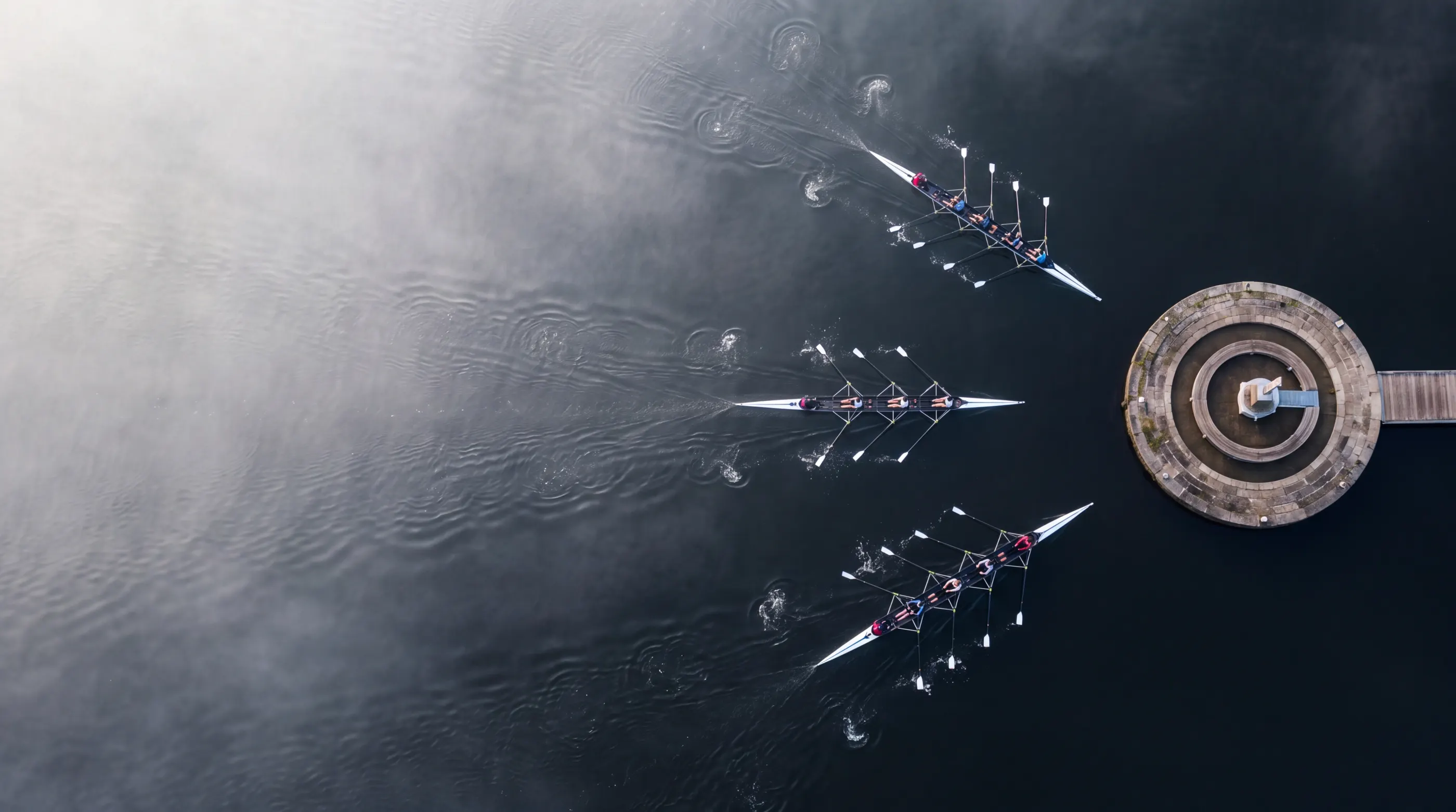 Aerial view of three rowing crews converging on a round pier